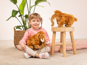 Child holding a plush toy next to a stool with another plush toy on it, in a home setting.