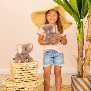 Young girl holding a plush elephant toy in a room with wicker baskets and a plant.
