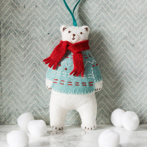 White polar bear wearing a red scarf and patterned sweater against a chevron-patterned wall.