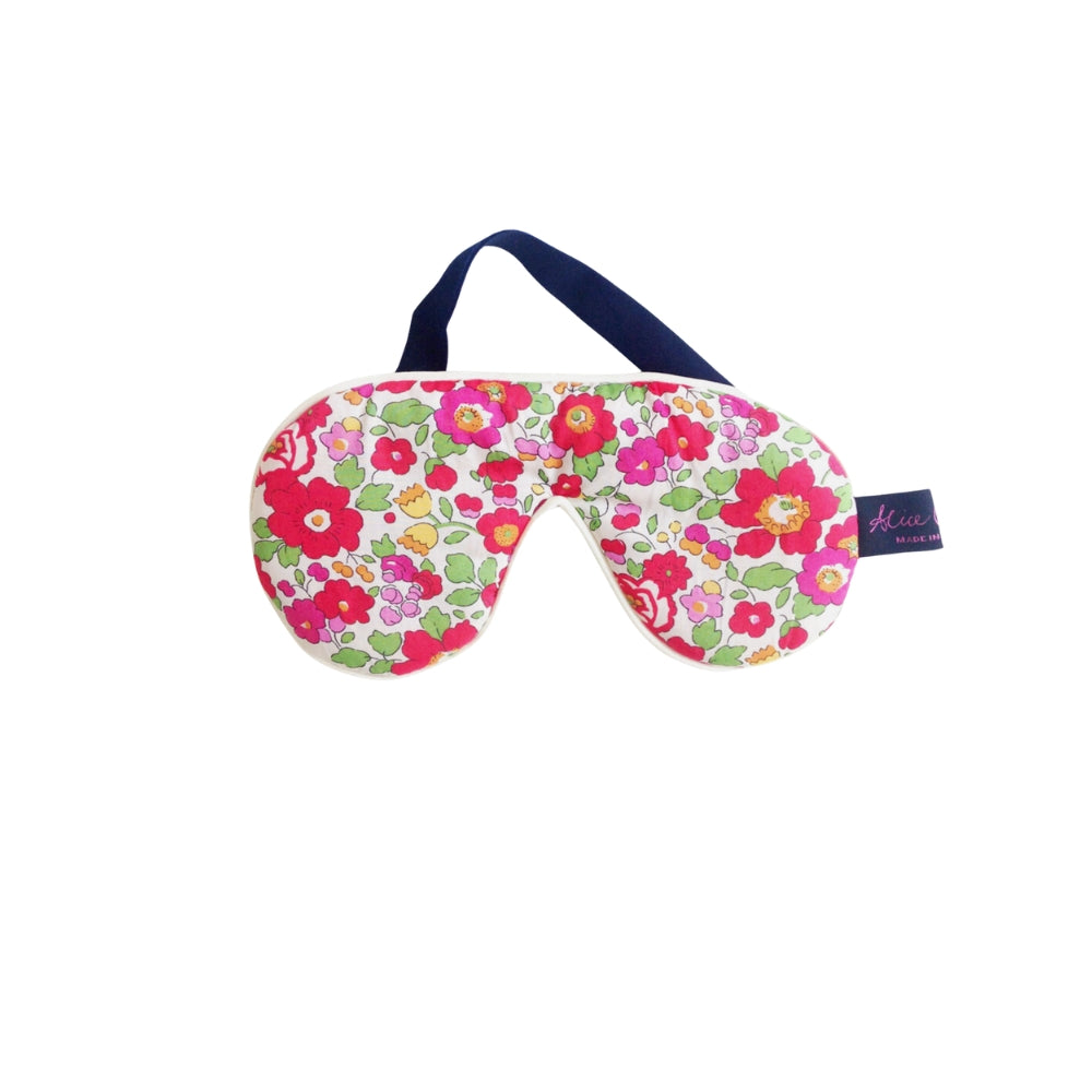 A floral sleep mask with a navy blue strap, featuring a vibrant pattern of pink, red, and green flowers on a white background, with a small brand tag on the side.