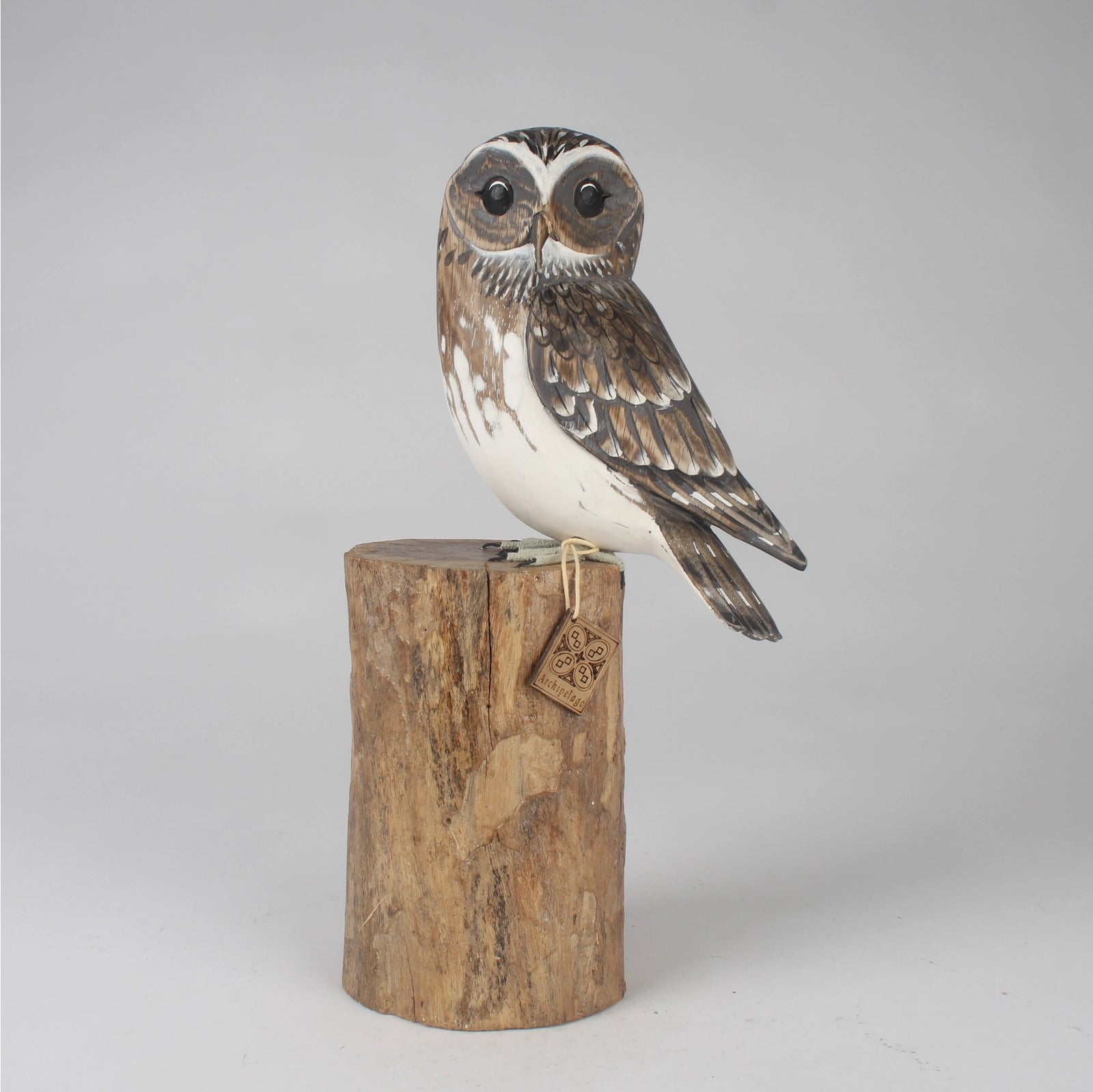 Wooden owl figurine on a cylindrical wooden base with a tag against a gray background