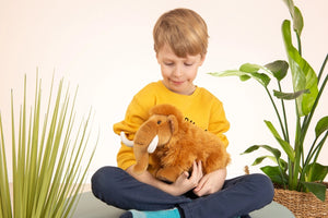 Child holding a plush lion toy in a room with plants