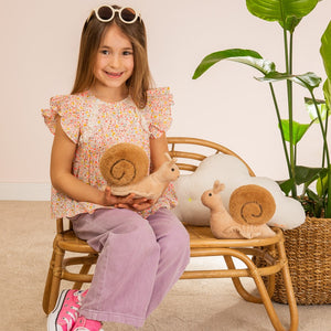 Young girl sitting on a chair holding a plush toy, with plants in the background