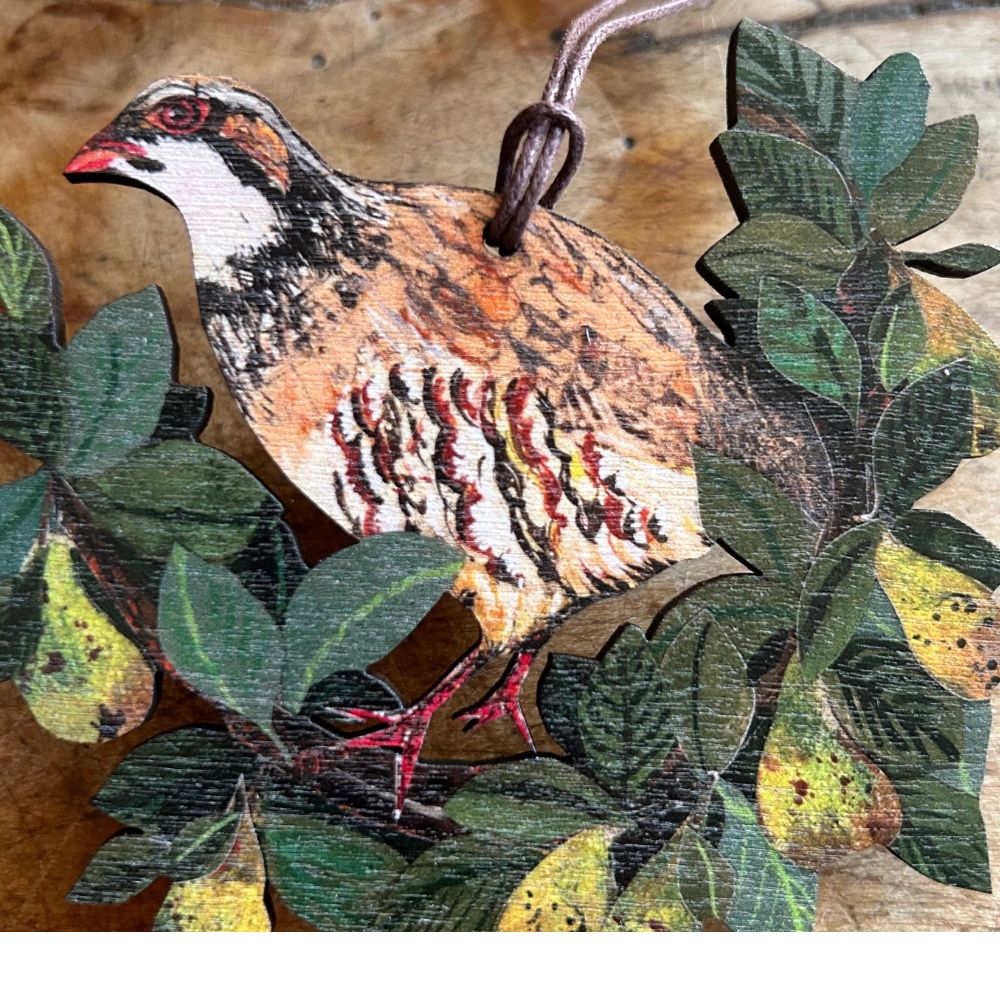 A hanging wooden decoration featuring a partridge in a pear tree with a branch and leaves in the background.