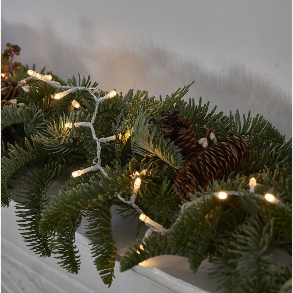 Decorative Christmas wreath with lights and pine cones on a plain background