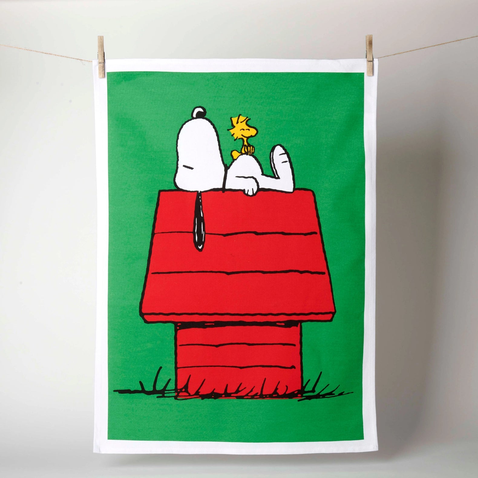 Tea towel with Snoopy and Woodstock on a red doghouse against a green background