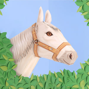 White horse head with a brown bridle surrounded by green leaves on a blue background